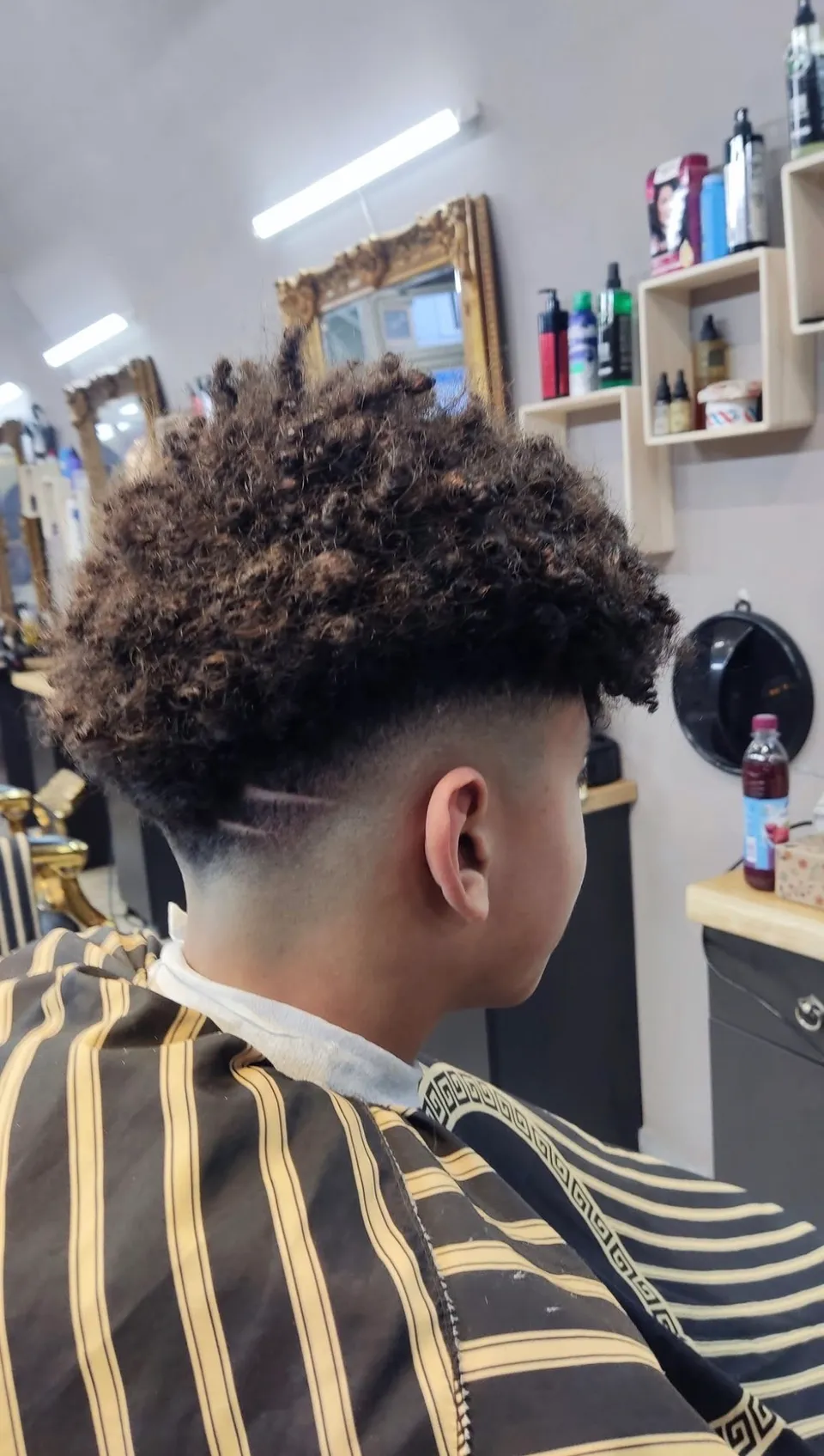 Lockiger Deckhaarschnitt mit hohem Fade und geschwungener Nackenlinie, von hinten fotografiert